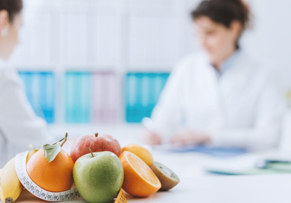 Professional nutritionist meeting a patient in the office and healthy fruits with tape measure on the foreground: healthy eating and diet concept